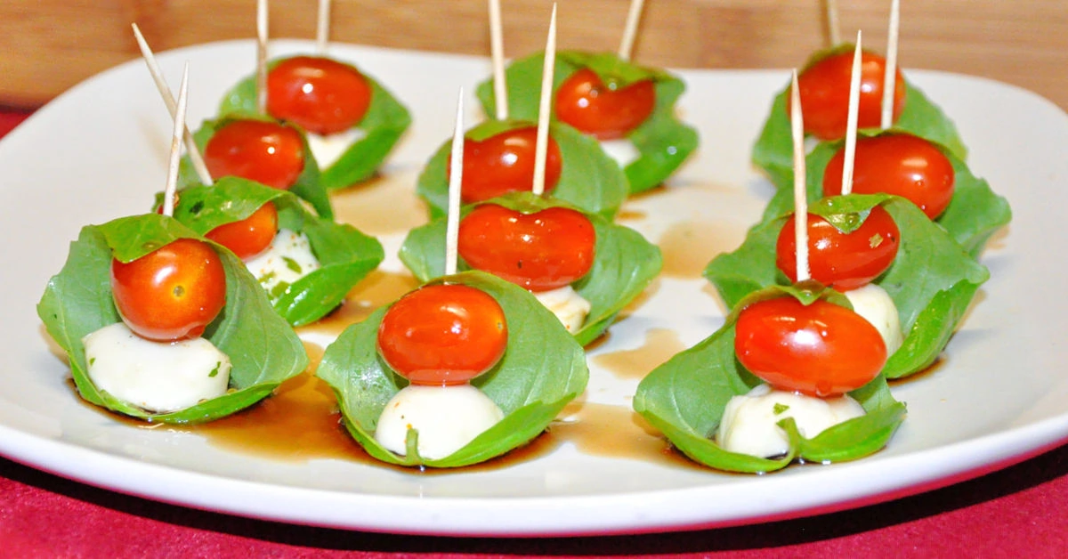 12 caprese skewers on a square white serving platter.