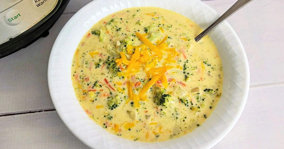 Broccoli Cheddar Soup served in a white bowl next to an Instant Pot on a white wood table.