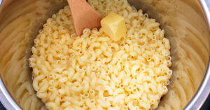 Cooked gluten free elbow noodles and butter being stirred together in Instant Pot inner pan.