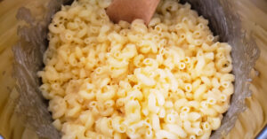Milk being stirred into gluten free elbow noodles in Instant Pot inner pan.