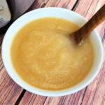 Bow of homemade applesauce with a wood ladle for serving.